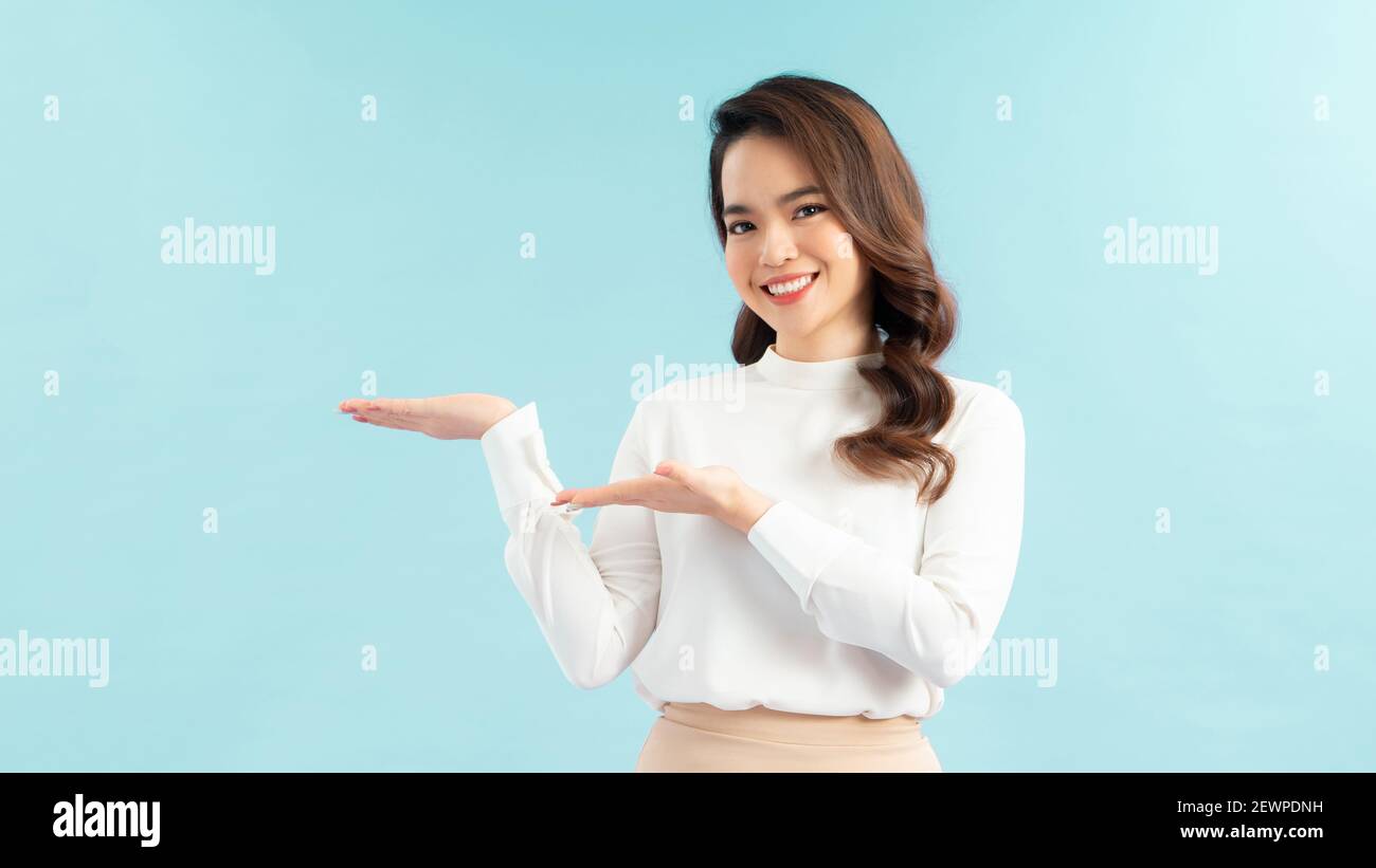 Portrait of Asian beautiful young girl raising both hands aside show something, isolated in blue background. Stock Photo