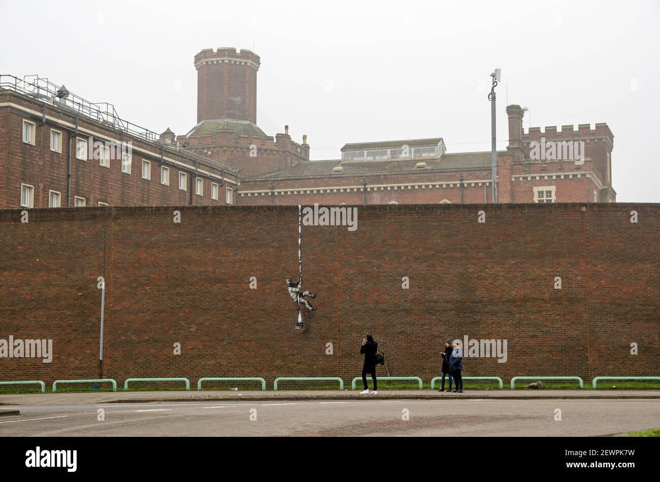 Reading, UK - March 3, 2021:  Local people admiring the graffiti art work Create Escape by Banksy showing a prisoner escaping from Reading Gaol. Stock Photo