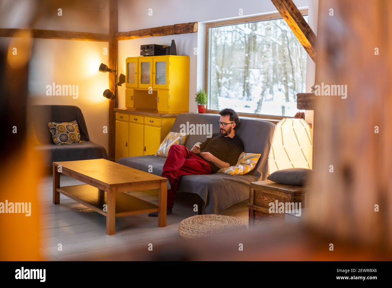 Young man sitting on couch at home, using smartphone Stock Photo