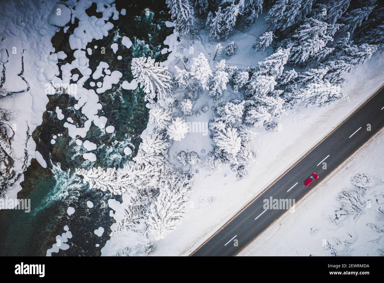 Car traveling on the snowy mountain road on side of frozen river and woods, aerial view, Switzerland, Europe Stock Photo