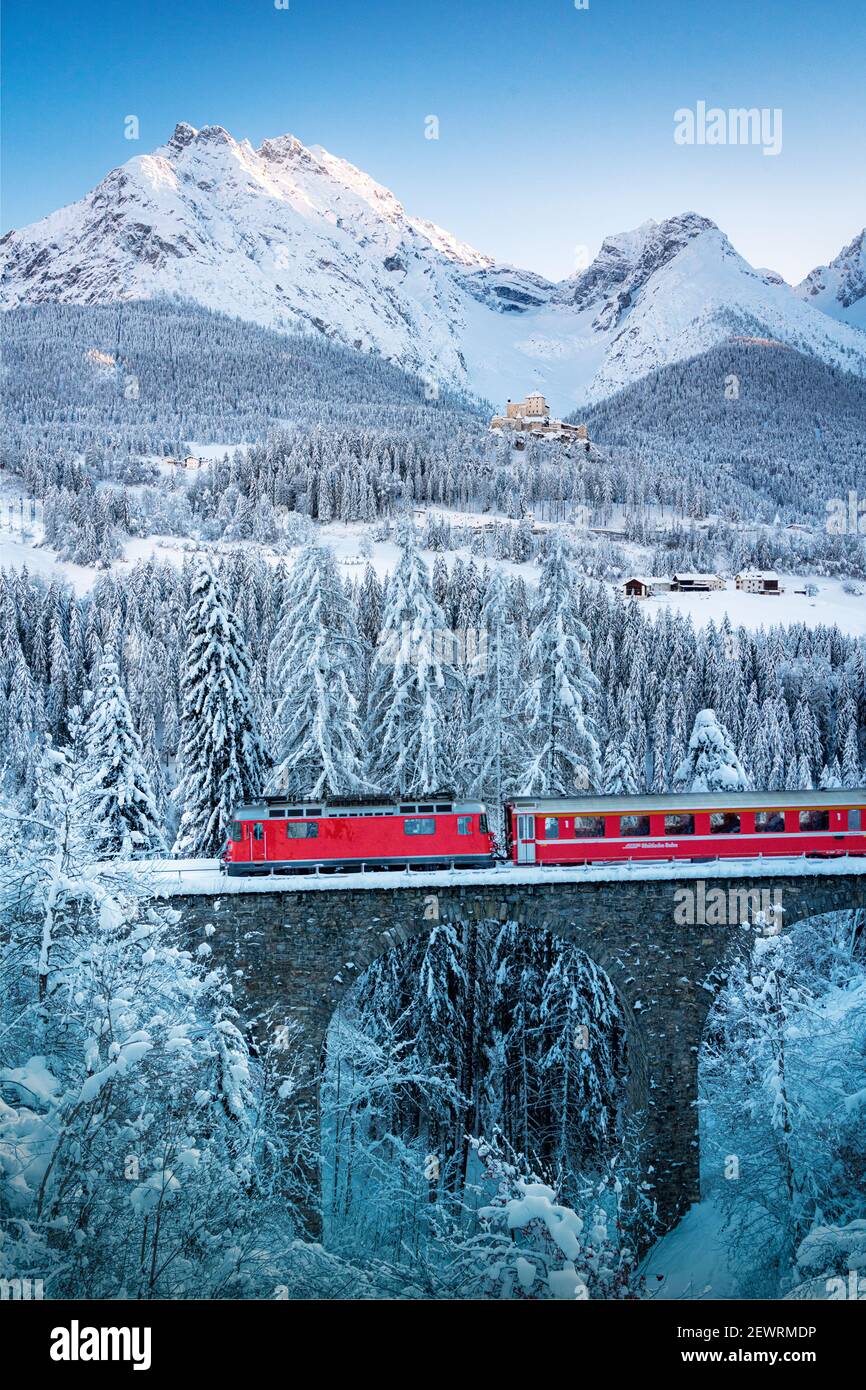 Bernina Express train in the winter forest covered with snow surrounding Tarasp Castle, Engadine, Graubunden Canton, Switzerland,  Europe Stock Photo