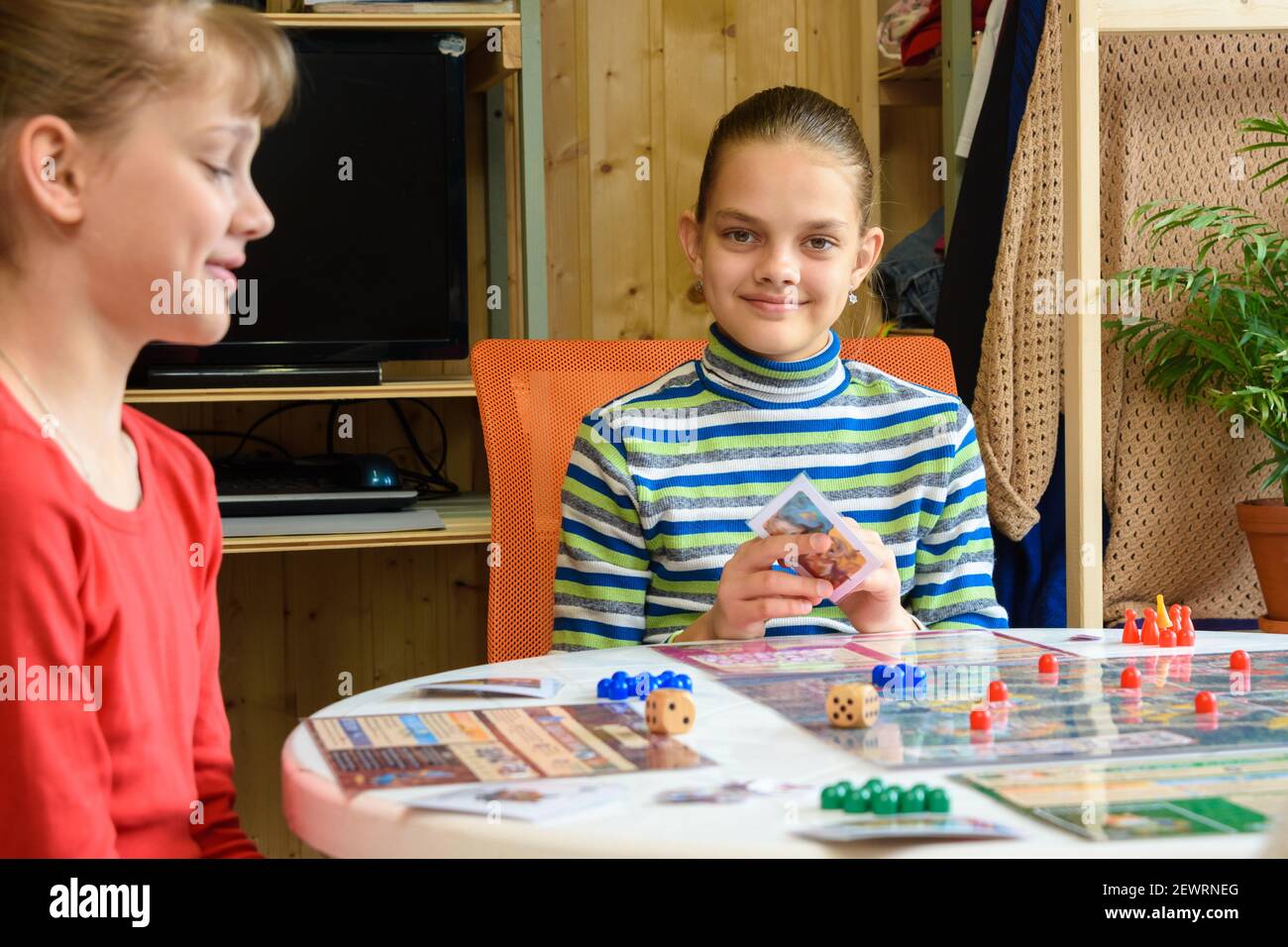 Children in a good mood are playing a board game, one of the girls looked into the frame Stock Photo