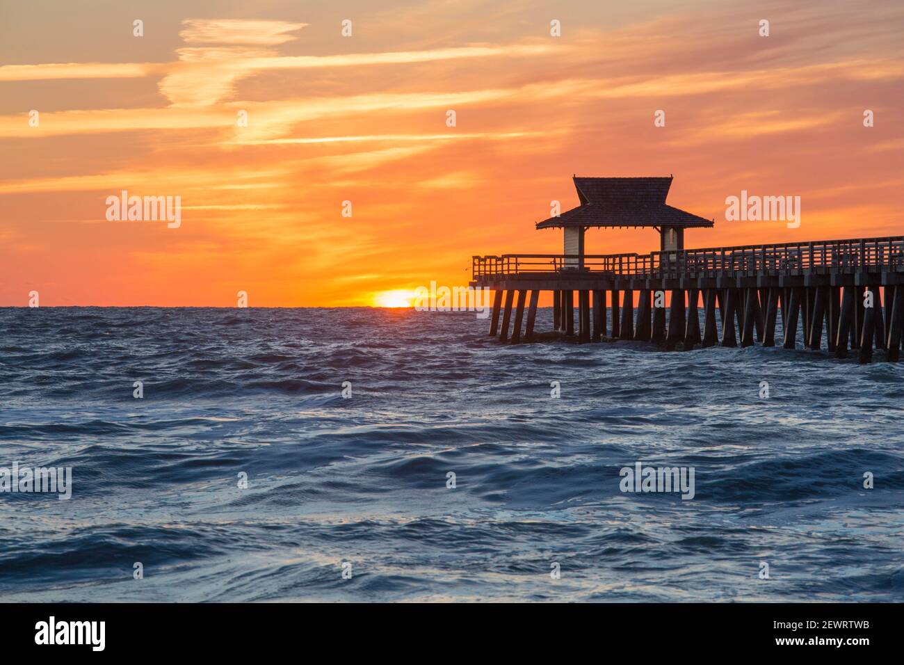 View across the Gulf of Mexico from beach beside Naples Pier, sunset, golden sky above horizon, Naples, Florida, United States of America Stock Photo