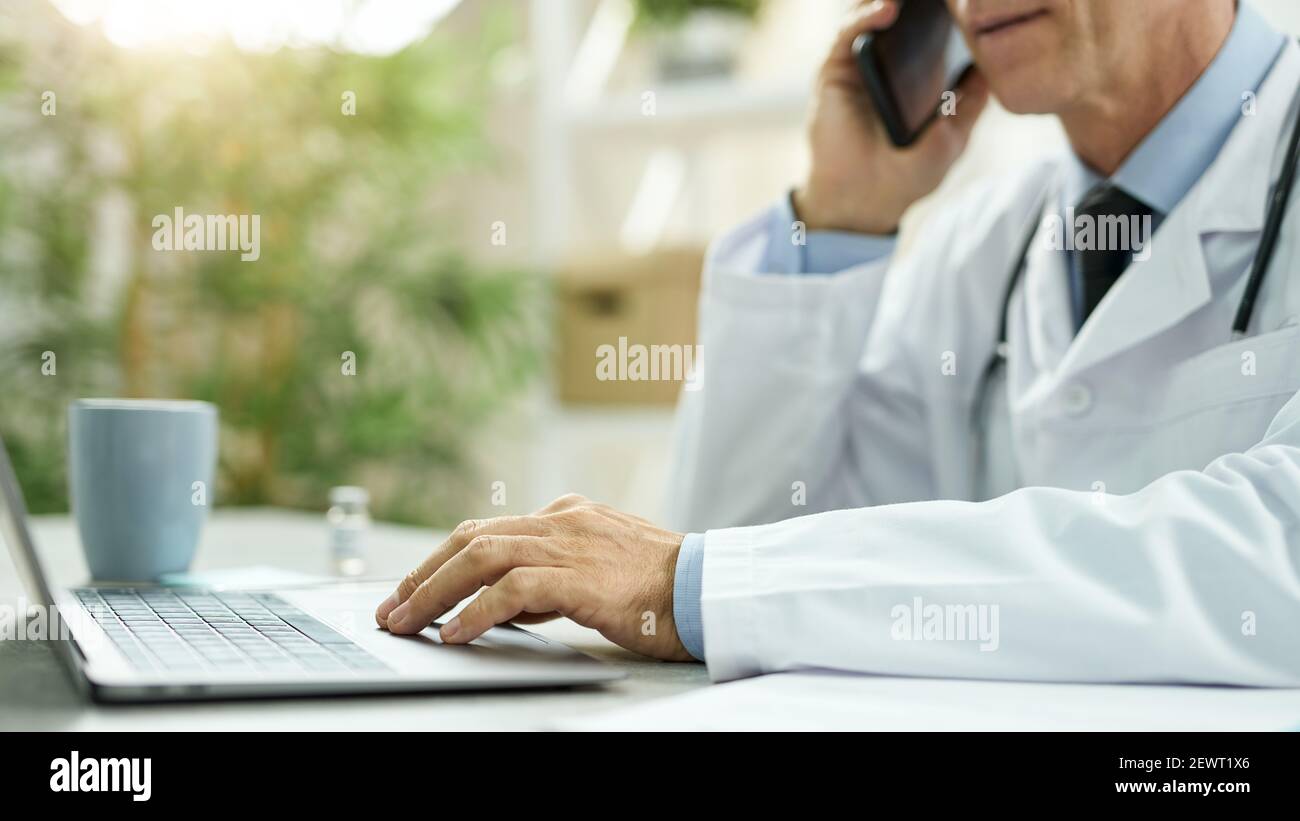 Doctor talking on mobile phone and using laptop at work Stock Photo