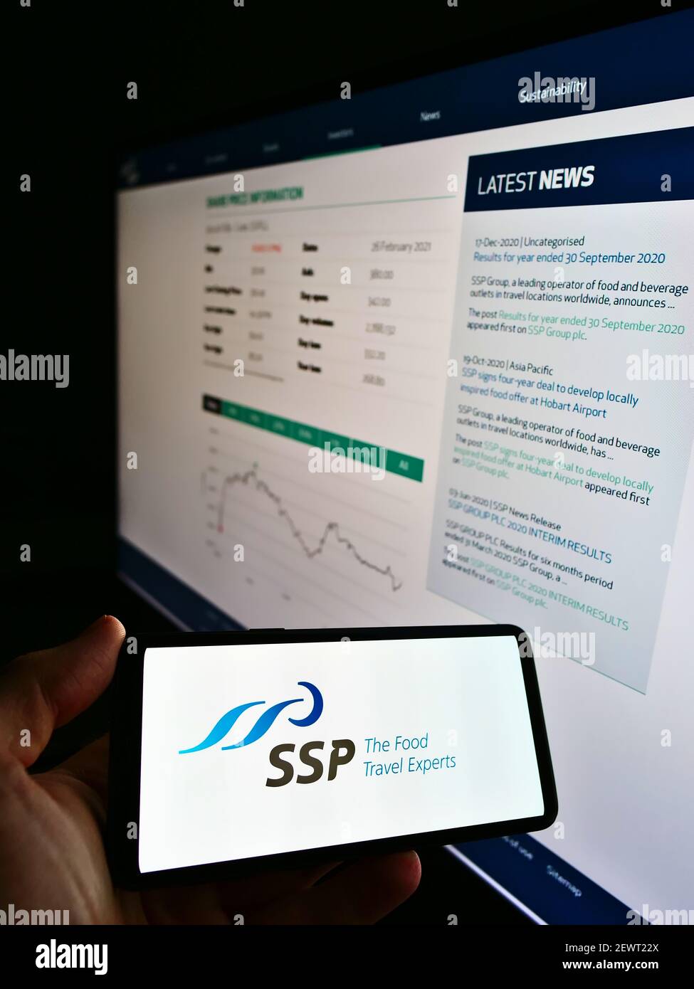 Person holding mobile phone with logo of British foodservice company SSP Group plc on screen in front of web page with chart. Focus on phone display. Stock Photo