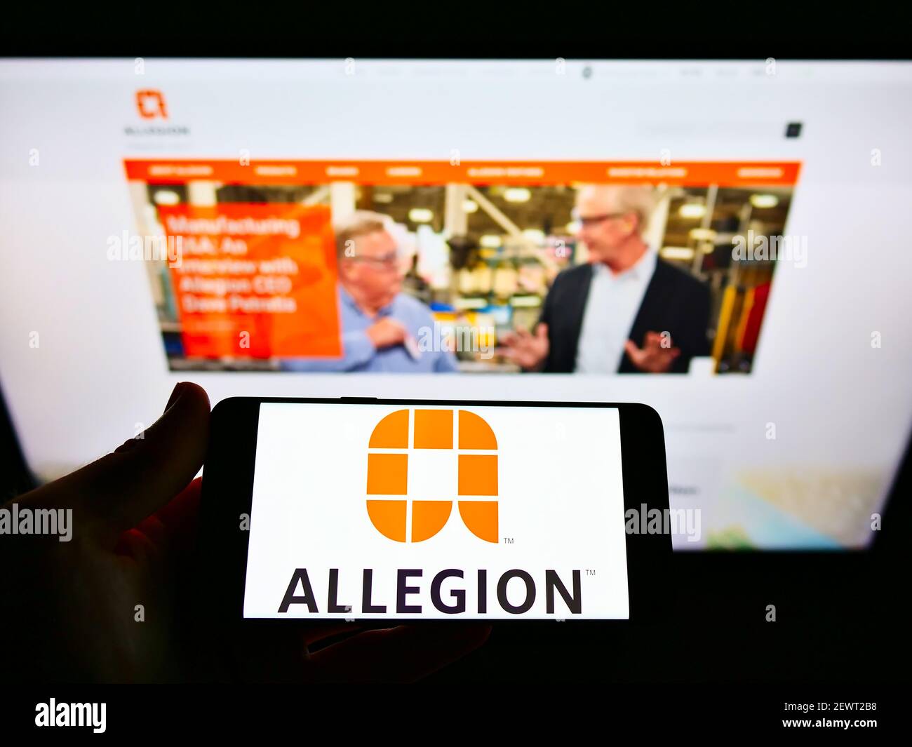 Person holding mobile phone with business logo of Irish security product company Allegion plc on screen in front of web page. Focus on phone display. Stock Photo