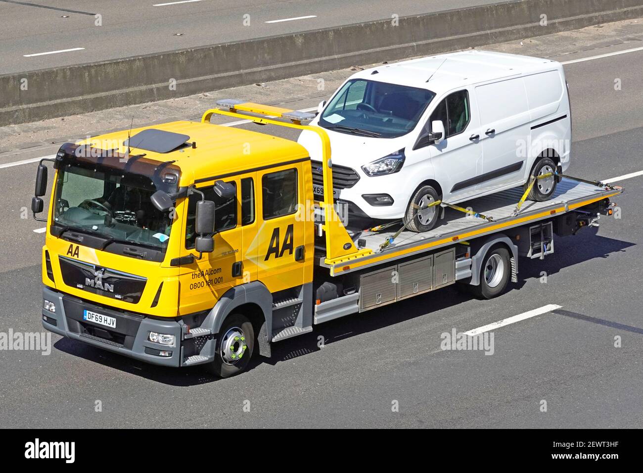Looking down from above side & front view AA MAN breakdown transporter pickup truck & white van secured by webbing restraints driving on UK motorway Stock Photo