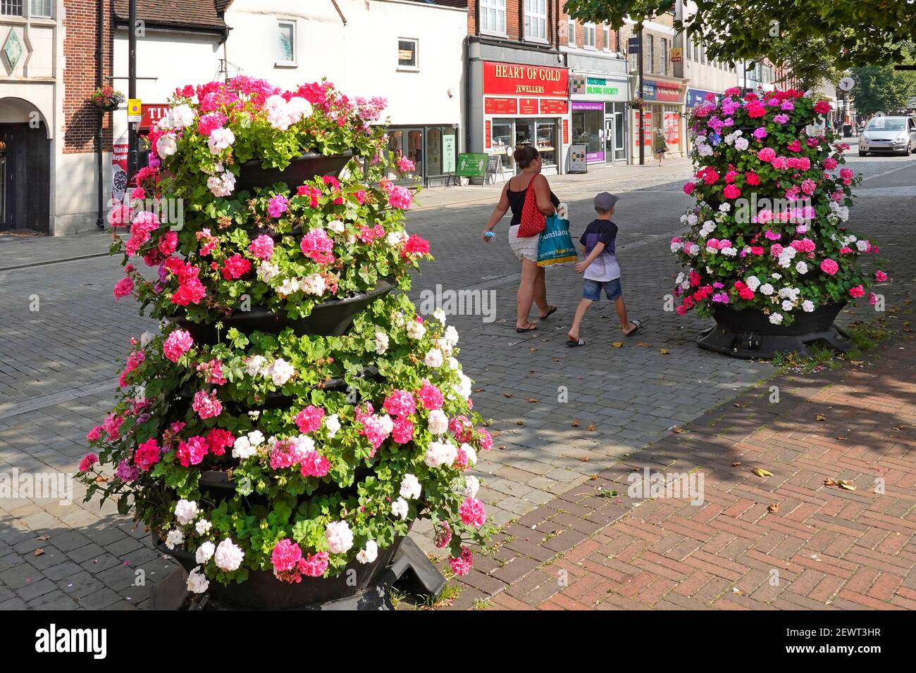 Mother holding Covid 19 coronavirus face mask in hand walking with young boy summer flowers in almost deserted Brentwood shopping High Street Essex UK Stock Photo