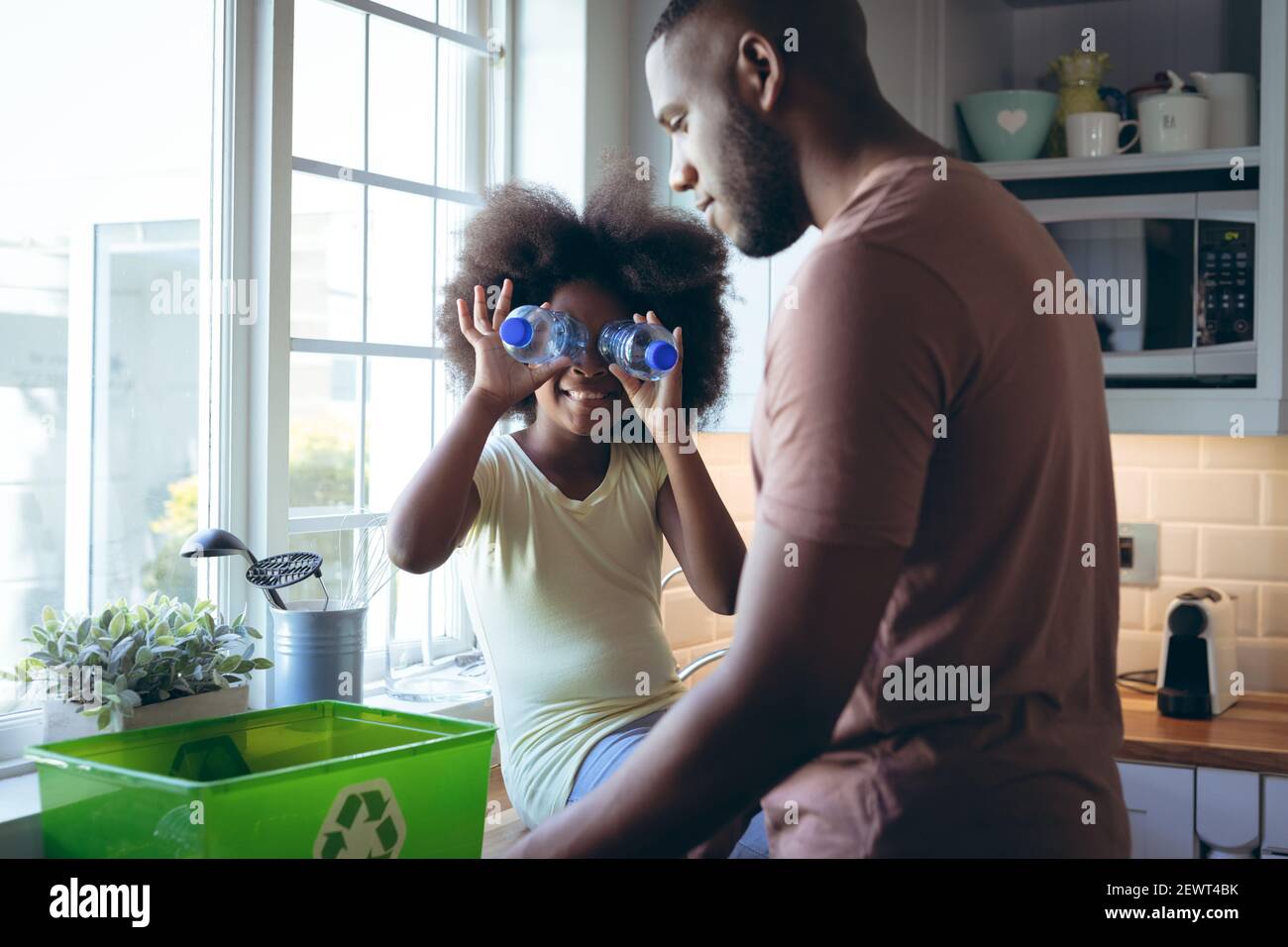 African american girl and her father sorting recycling together in kitchen Stock Photo