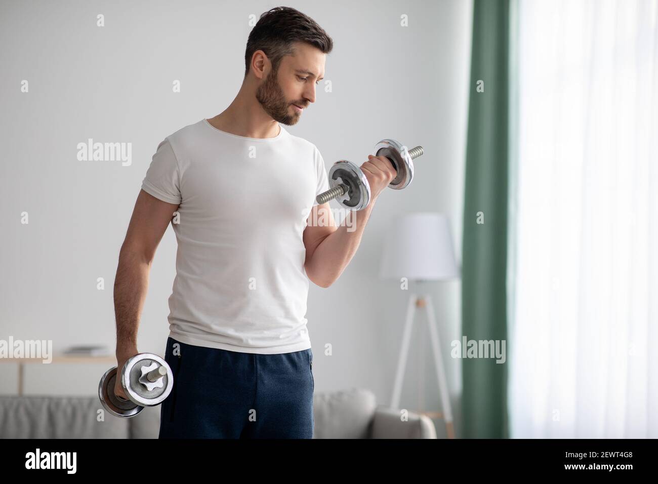 Closeup of handsome bearded man doing dumbbell workout at home Stock Photo