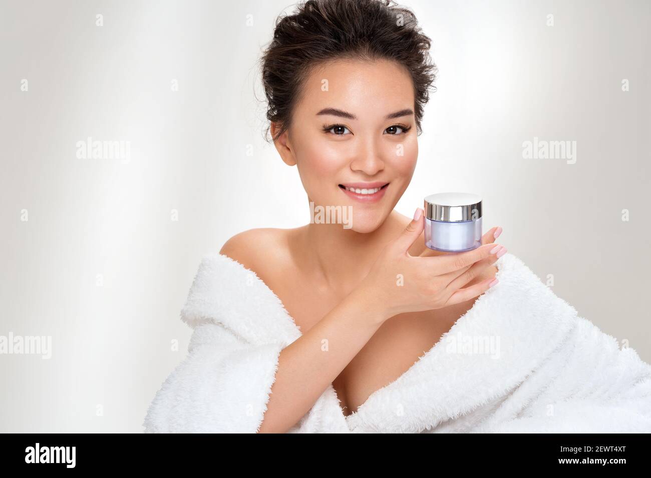 Woman holds jar with cosmetic cream. Photo of asian woman after shower