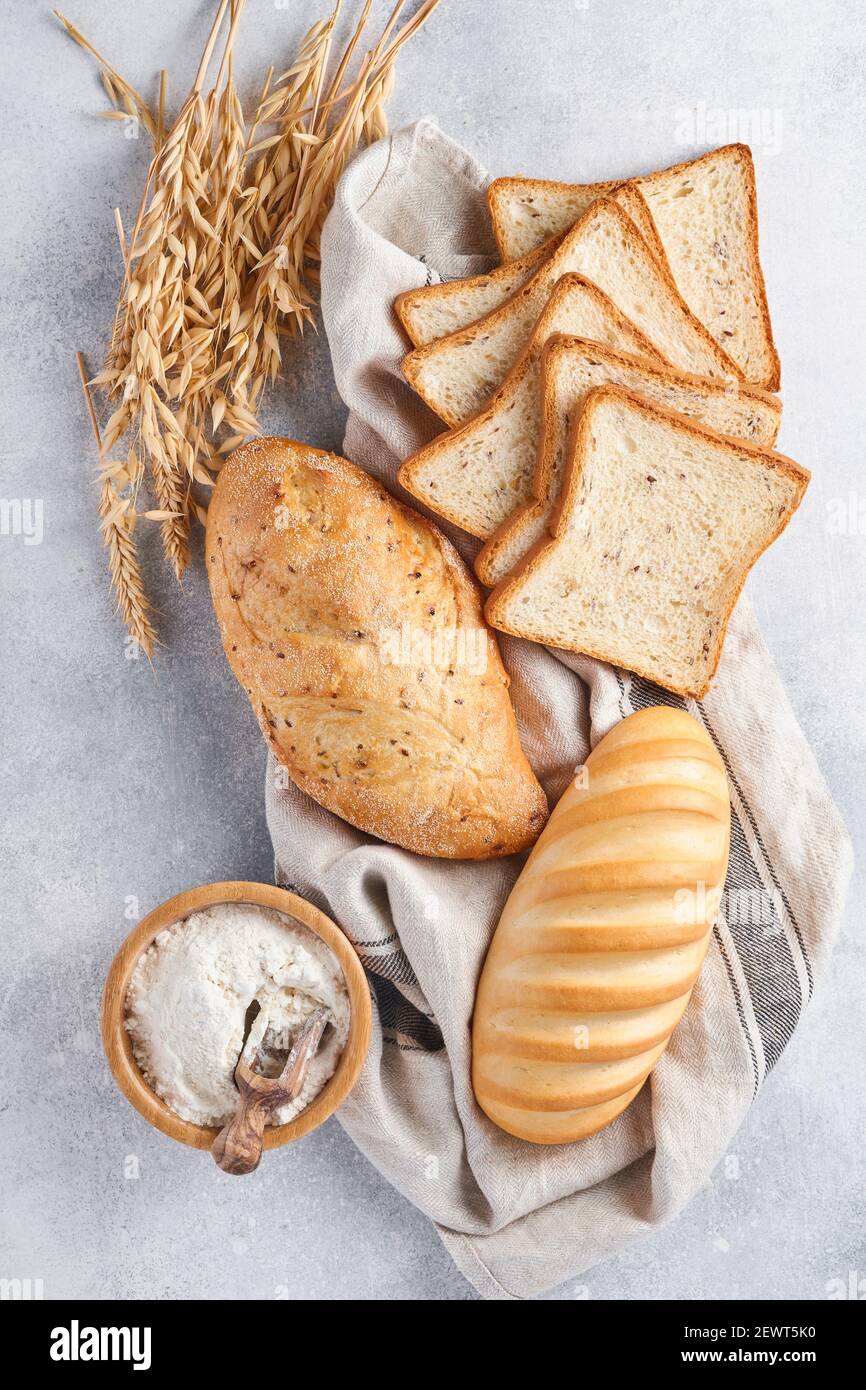 Various crispy breads and buns, wheat flour and ears on light gray