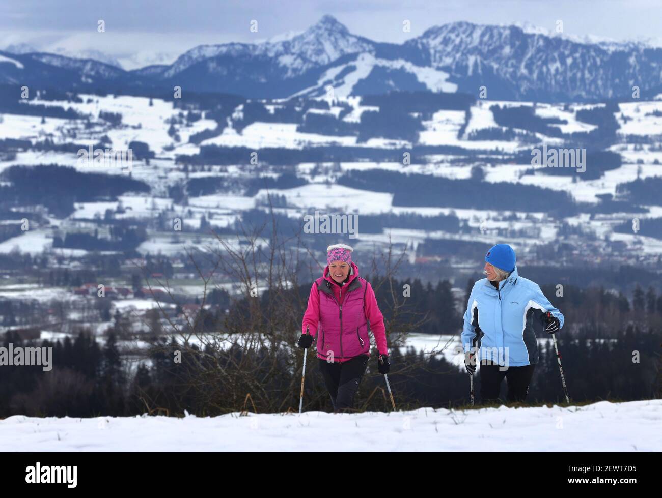 16 February 2021, Bavaria, Wiggensbach: Ida-Anna Braun (r), chairwoman of the Kempten Kneipp Association, and Monika Weitnauer, secretary and Nordic walking leader of the association, walk through the snow while Nordic walking in front of the panorama of the Alps. (to dpa 'Kneipp associations fight for image and members in anniversary year') Photo: Karl-Josef Hildenbrand/dpa Stock Photo
