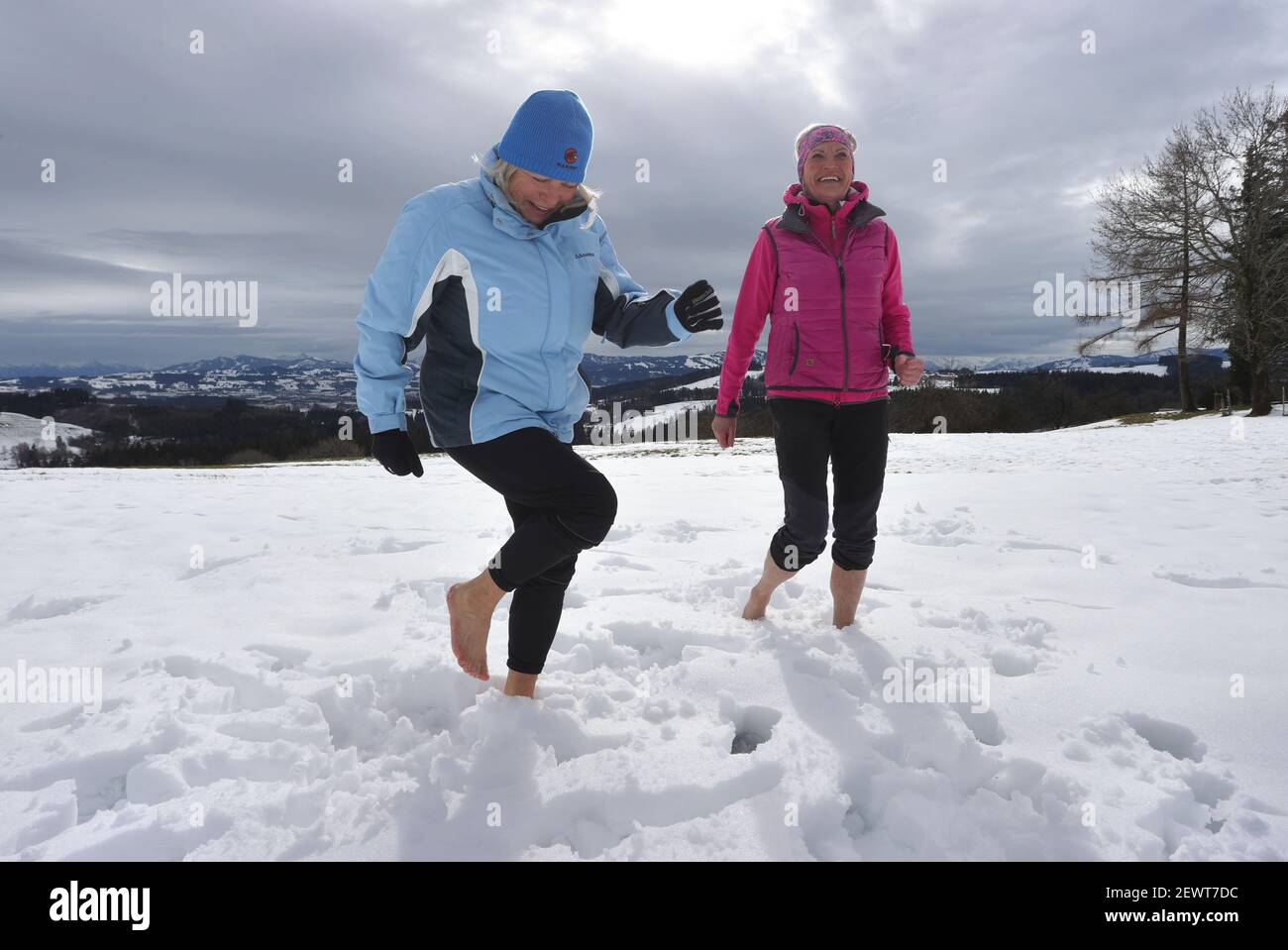 16 February 2021, Bavaria, Wiggensbach: Ida-Anna Braun (l), chairwoman of the Kempten Kneipp Association, and Monika Weitnauer, secretary and Nordic walking leader of the association, walk barefoot through the snow in front of the panorama of the Alps. (to dpa 'Kneipp associations struggle for image and members in anniversary year') Photo: Karl-Josef Hildenbrand/dpa Stock Photo