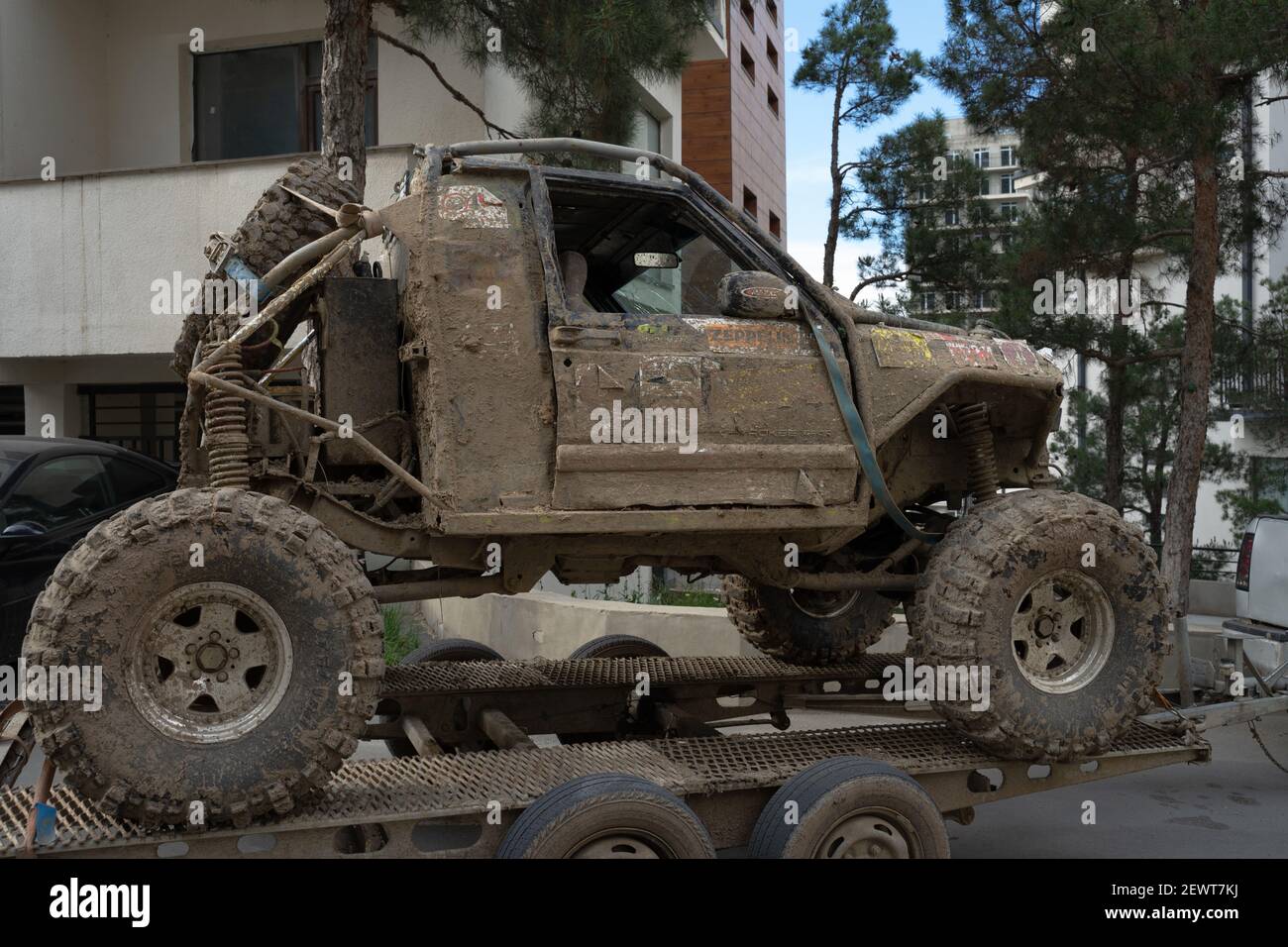 The dirty, completely covered with mud off road vehicle with broken window on the towing platform in the city. Stock Photo