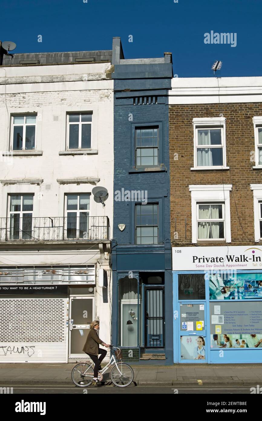 with dark-painted exterior, what is said to be the narrowest house in london seen with a a female cyclist passing, shepherds bush, london, england Stock Photo