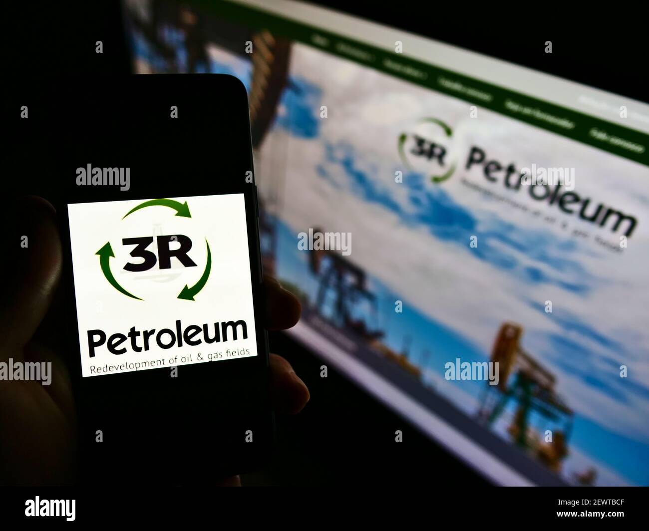 Person holding smartphone with logo of Brazilian oil and gas company 3R Petroleum S.A. on screen in front of website. Focus on phone display. Stock Photo
