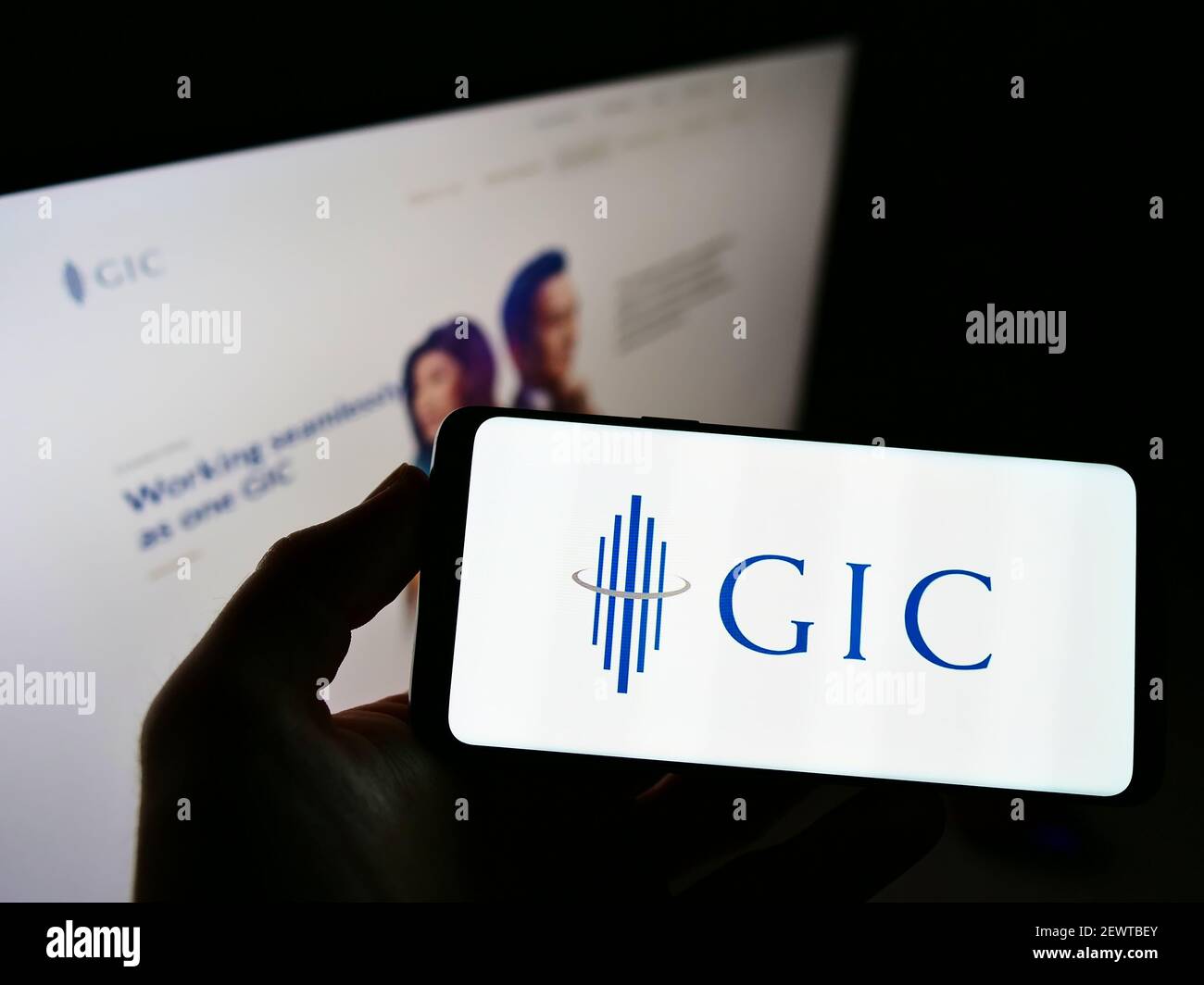 Person holding mobile phone with logo of Singaporean sovereign wealth fund GIC Private Limited on screen in front of webpage. Focus on phone display. Stock Photo