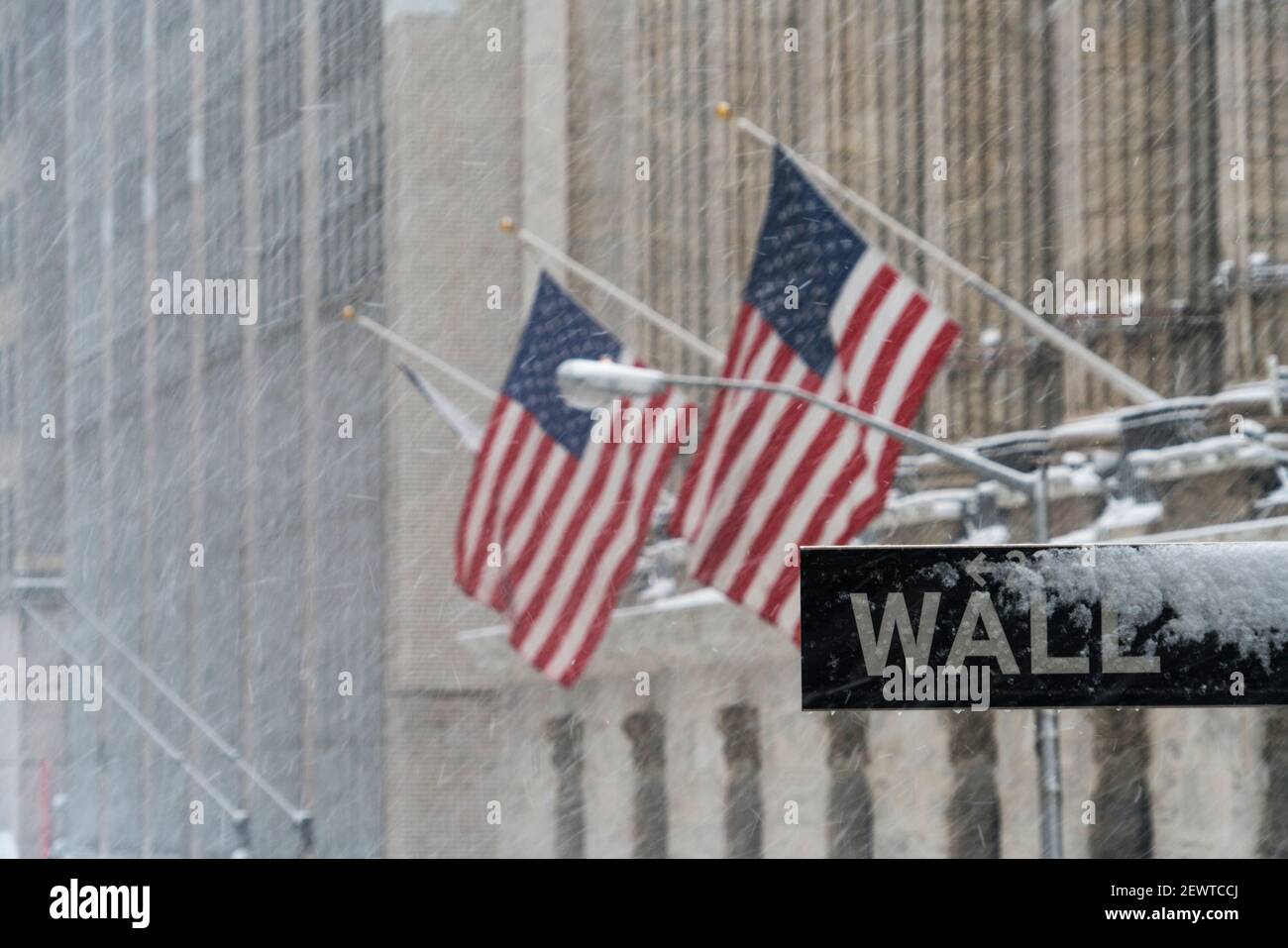 Wall Street road sign stands at front of New York Stock Exchange during the winter snowstorm at Lower Manhattan New York City NY USA. Stock Photo