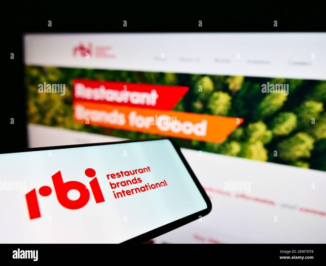 Person holding smartphone with logo of food company Restaurant Brands International Inc. (RBI) on screen in front of website. Focus on phone display. Stock Photo