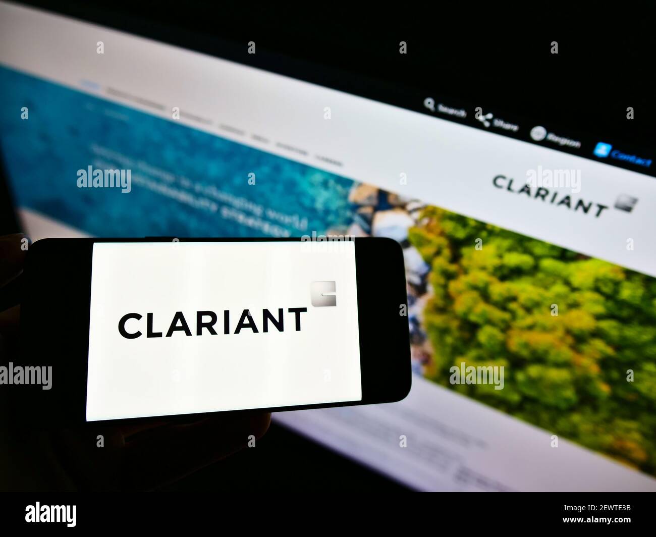 Person holding smartphone with logo of Swiss specialty chemicals company Clariant AG on screen in front of website. Focus on phone display. Stock Photo
