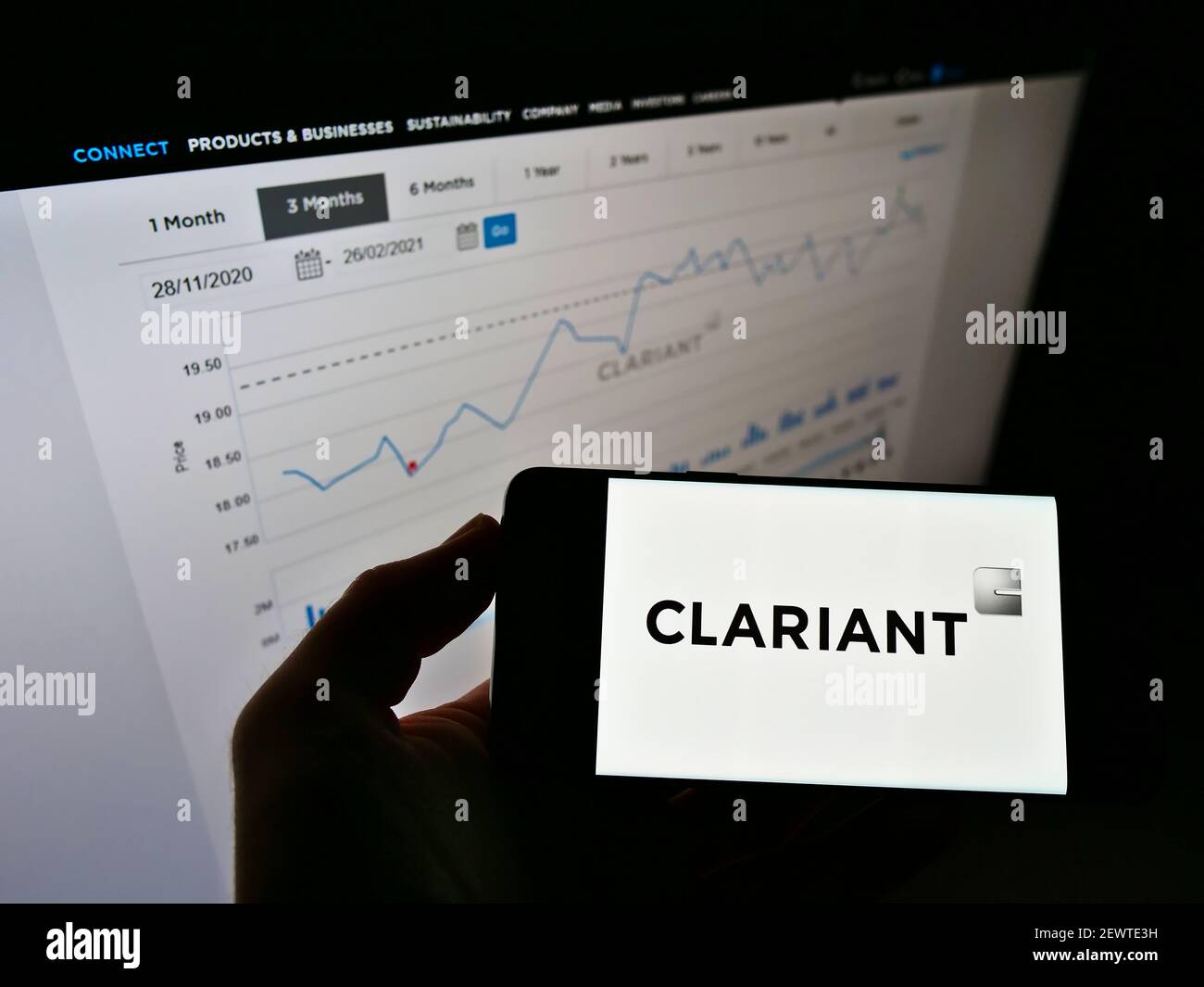 Person holding cellphone with logo of Swiss specialty chemicals company Clariant AG on screen in front of website with chart. Focus on phone display. Stock Photo