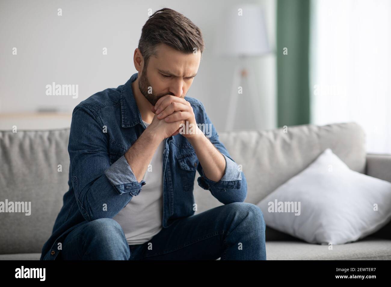 Upset bearded man sitting on sofa in living room Stock Photo
