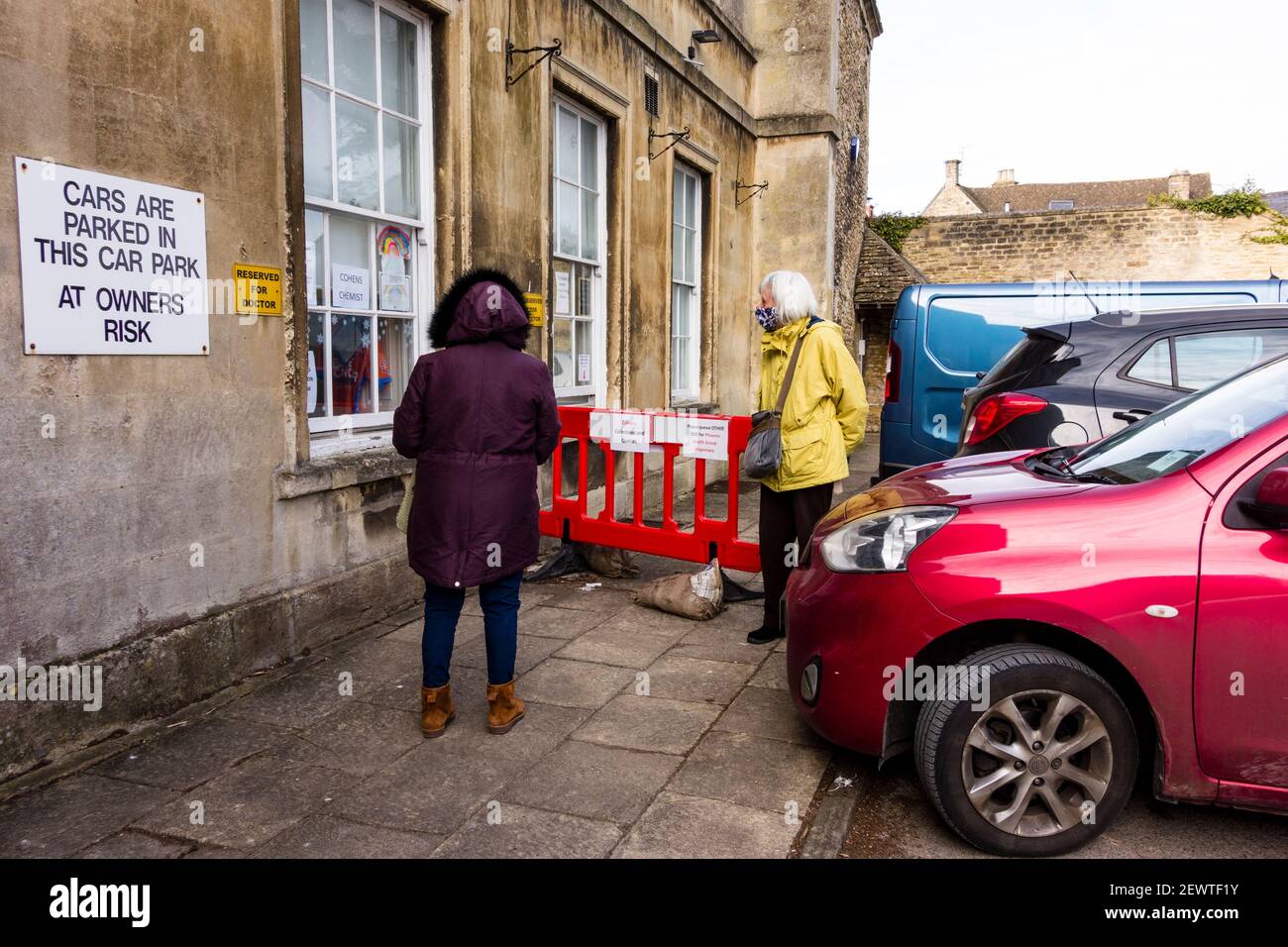 Two people waiting to collect their prescriptions through collect point window, Tetbury, Gloucestershire, UK Stock Photo