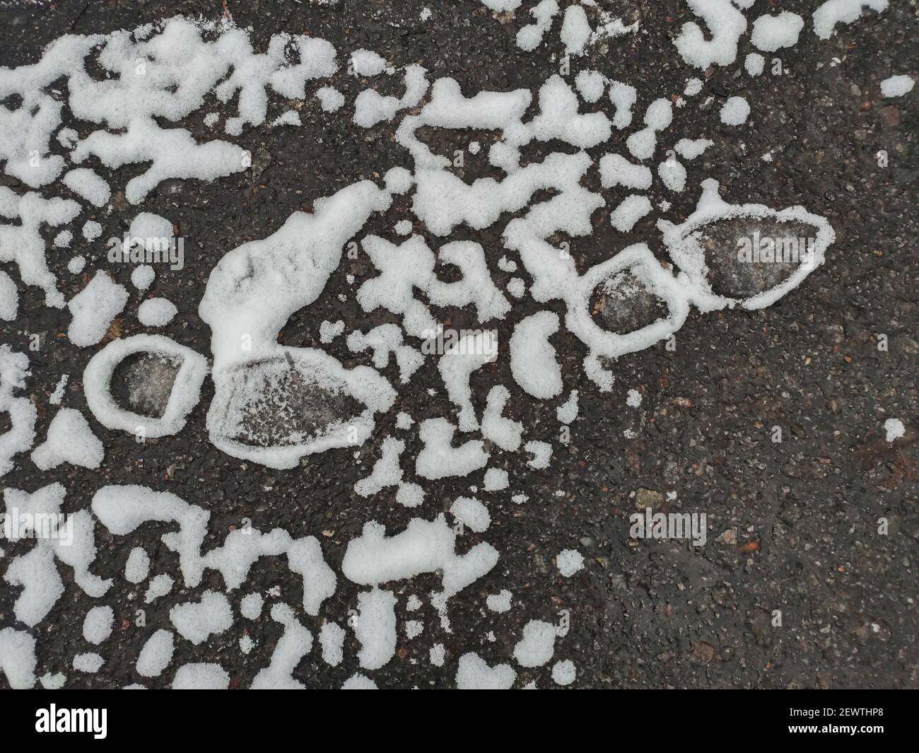 Beautifully melting snow around footprints on the asphalt Stock Photo