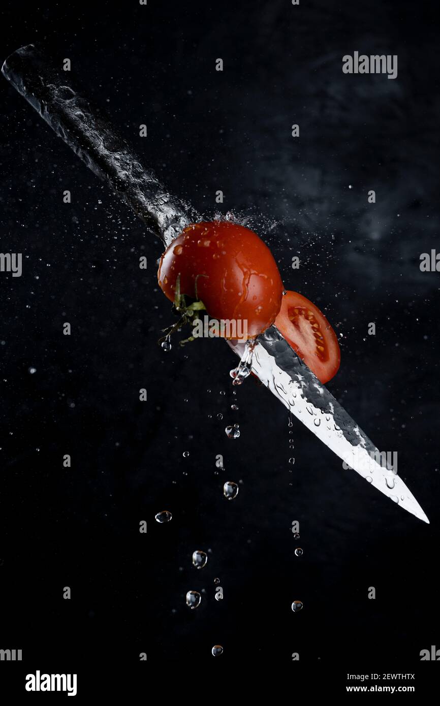 Fresh tomato cutting with a knife and flying in motion on the black