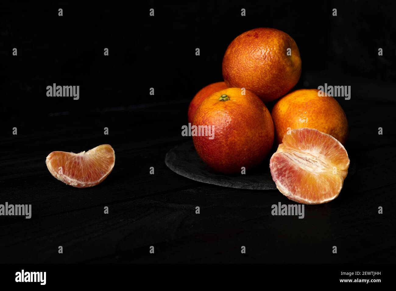 Whole and halved red oranges on black surface. Stock Photo