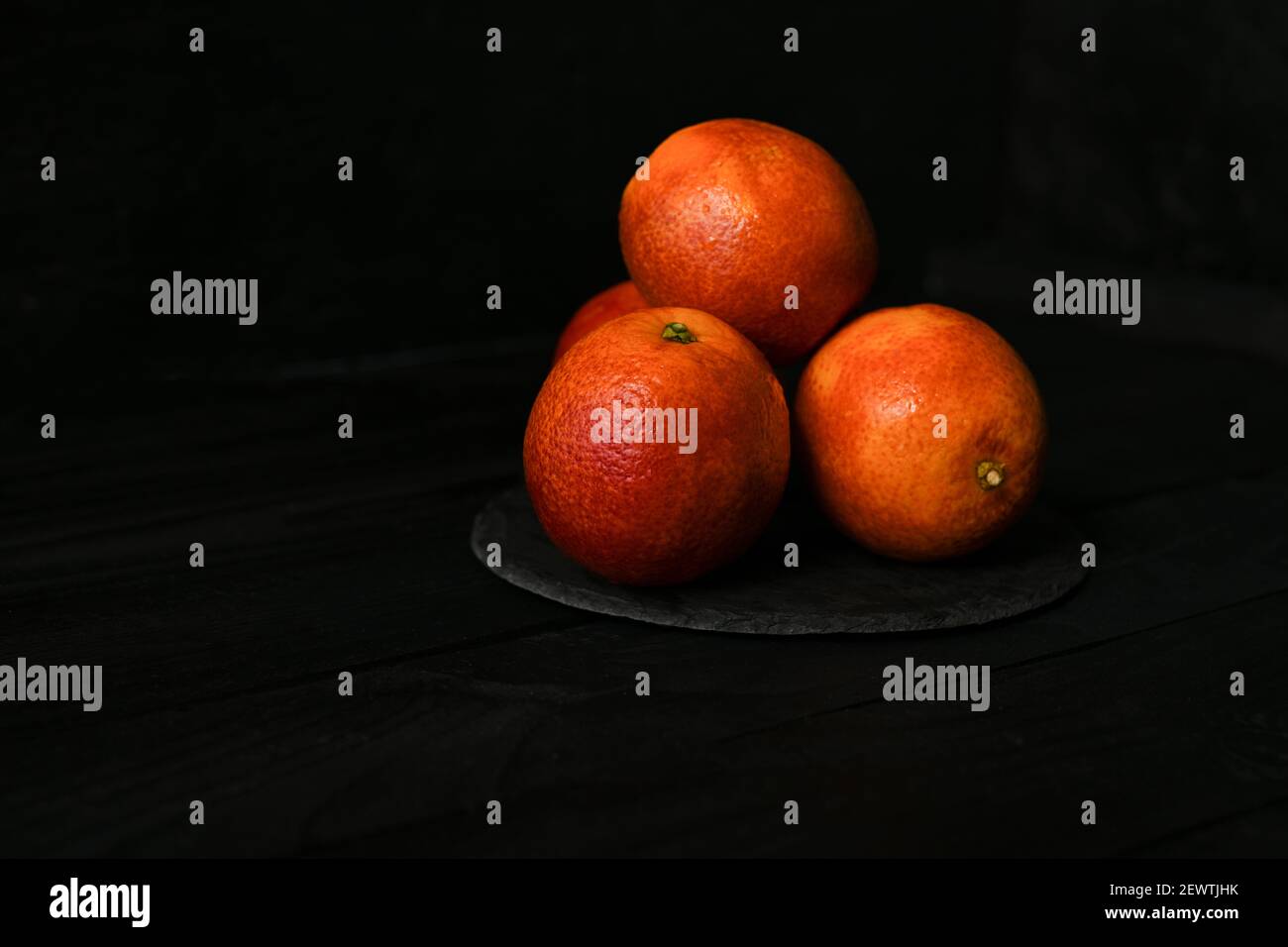Whole and halved red oranges on black surface. Stock Photo