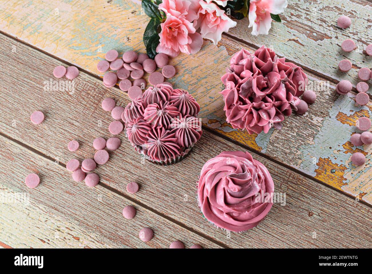 Three chocolate cupcakes with pink butter cream. Next to Ruby chocolate callets. Stock Photo