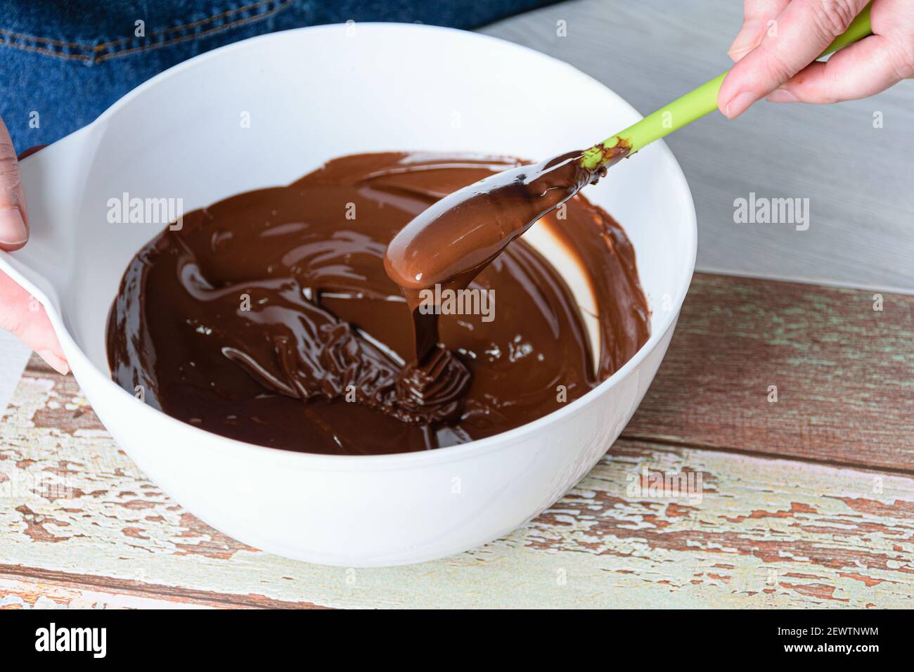 Confectioner tempering chocolate with a spatula in a white bowl Stock