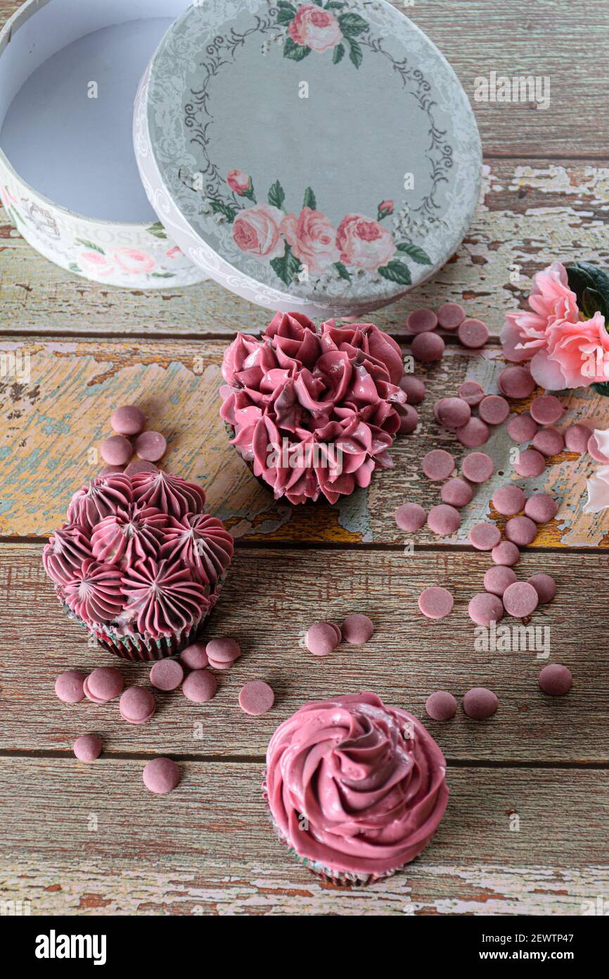 Chocolate cupcakes with pink butter cream, next to Ruby chocolate callets and a round box. Stock Photo
