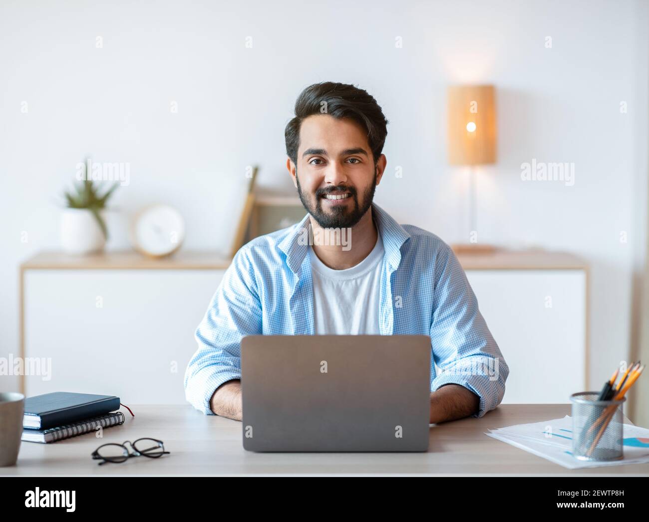 Freelance Lifestyle. Portrait Of Smiling Eastern Guy Sitting At Desk With Laptop Stock Photo