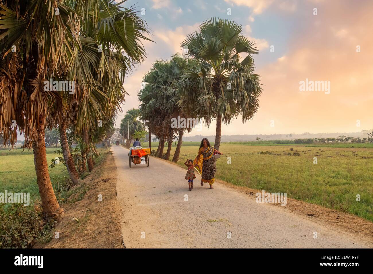 Rural woman with her kid walking down an unpaved village road with view