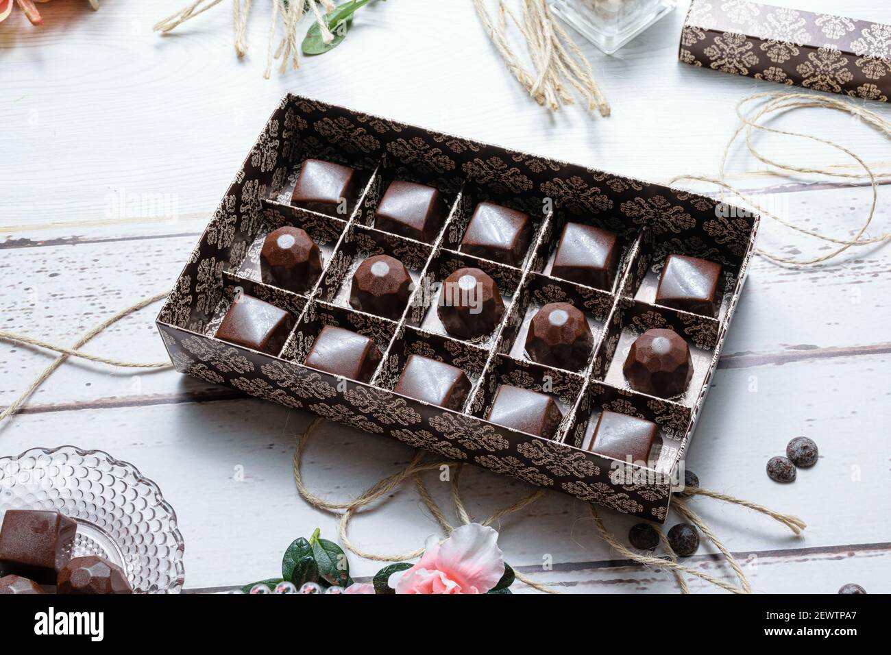 Brown box with several chocolate candies, on twine rope. Next to ...