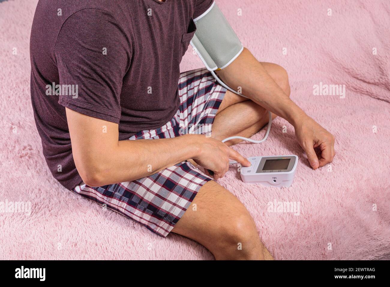 A 50-year-old man measures his blood pressure with a blood pressure monitor at home, sitting on his bed in his home clothes. Surprised by the instrume Stock Photo