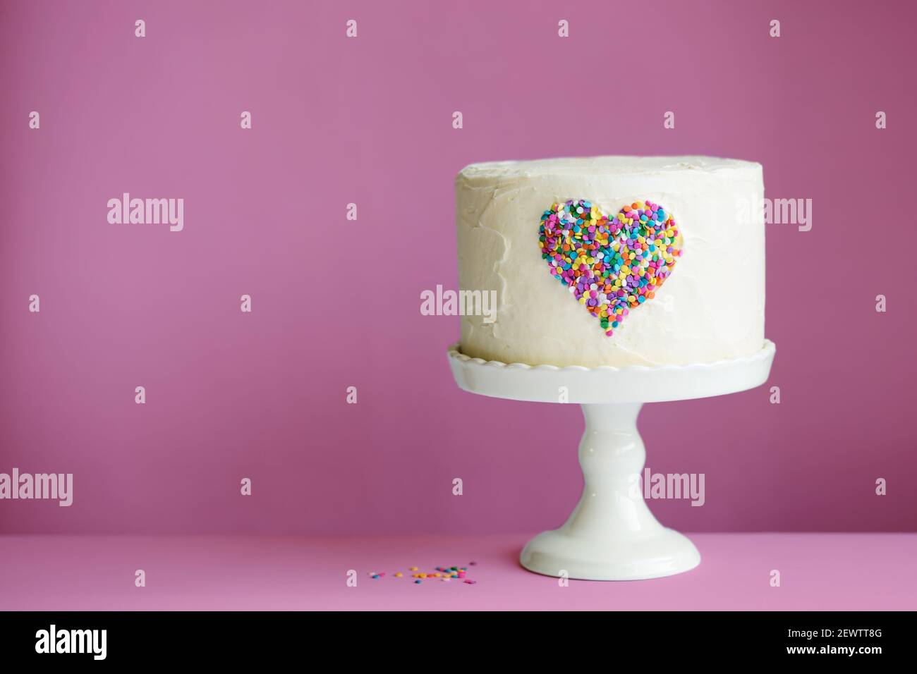 White Valentines cake with colorful heart made of sprinkles on a pink background Stock Photo