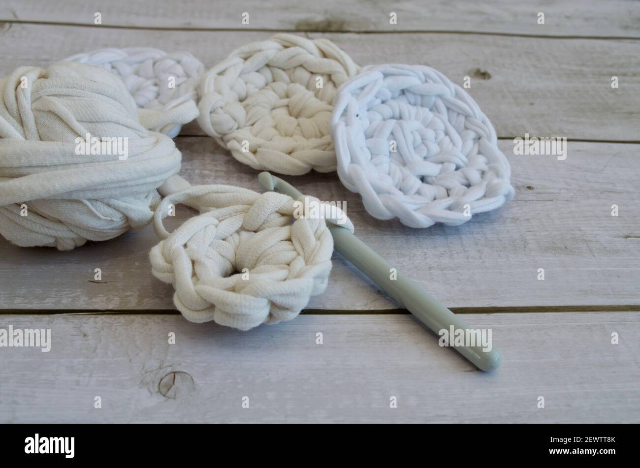 Skein of ribbon yarn with crochet hooks and crocheted coasters in light color Stock Photo