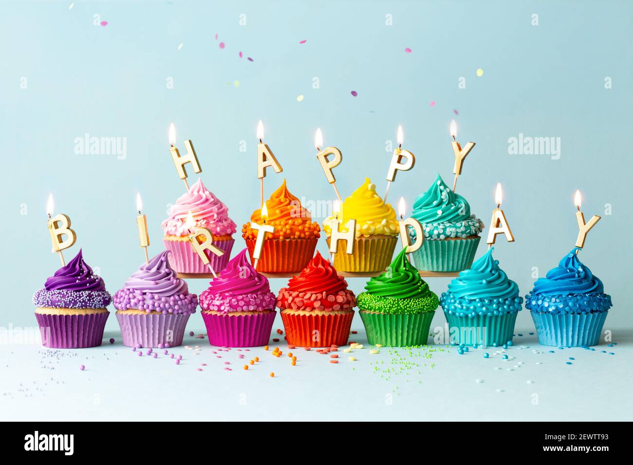 Rainbow colored cupcakes with birthday candles spelling happy birthday Stock Photo
