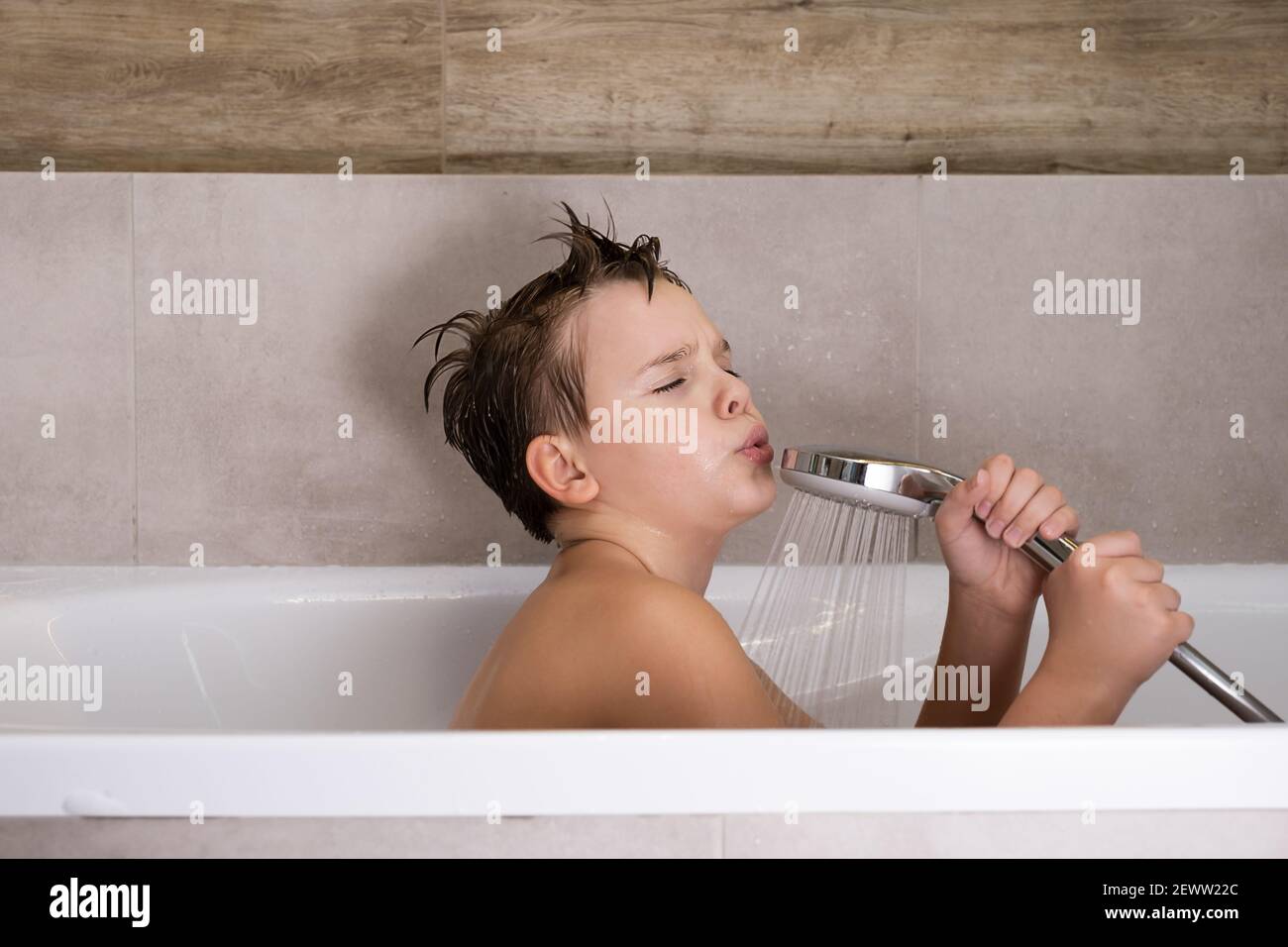 Happy boy holding shower head and singing while washing in bathroom