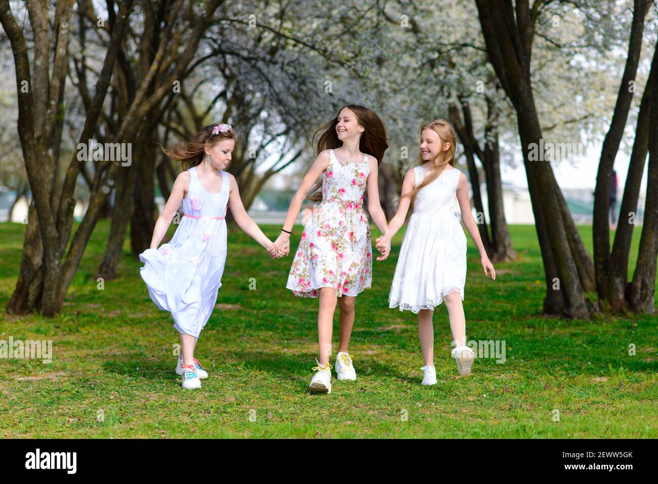 Three adorable girls in dresses hold hands in a circle holding hands ...