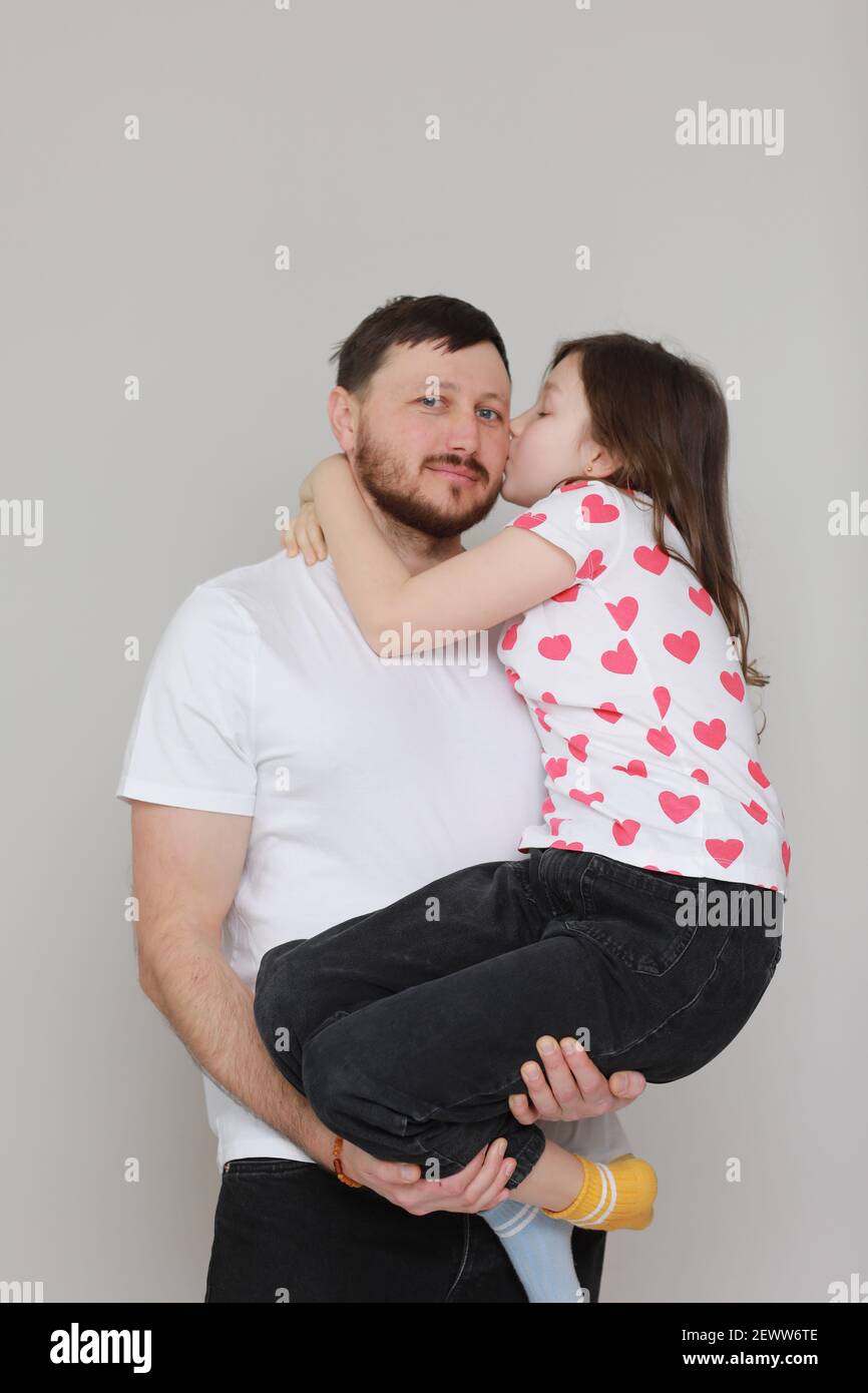 young dad holds his little daughter in his hands. father hugging his child  with love and child kiss him. man in white t-shirt and girl in t-shirt with  Stock Photo - Alamy