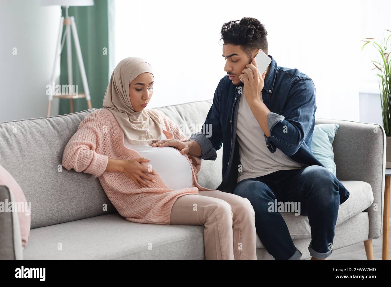 Pregnant Muslim Lady Having Prenatal Contractions At Home, Her Husband Calling Emergency Stock Photo