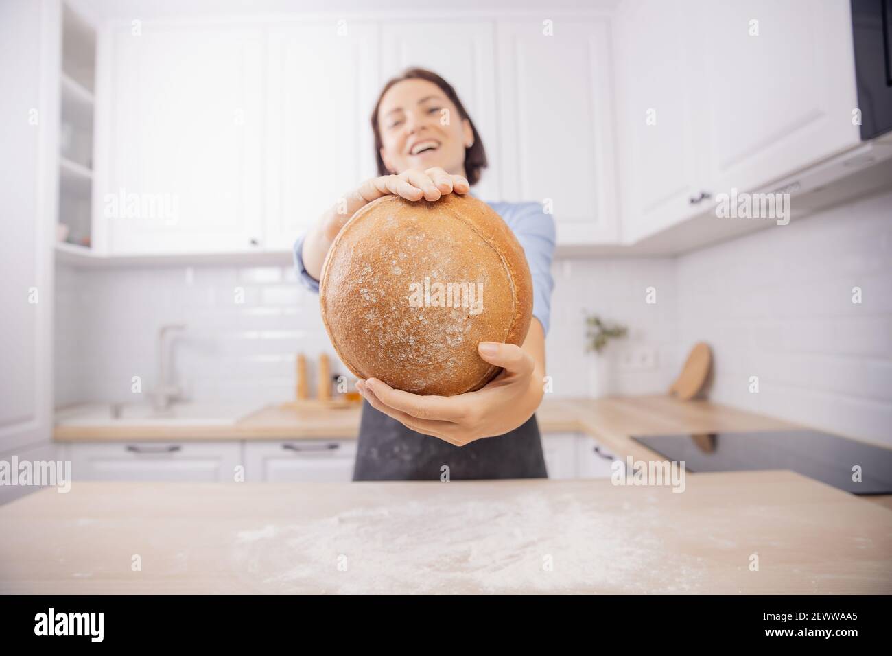 Baker hand wheaten Round loaf of bread lies on table with flour, background white kitchen. Stock Photo
