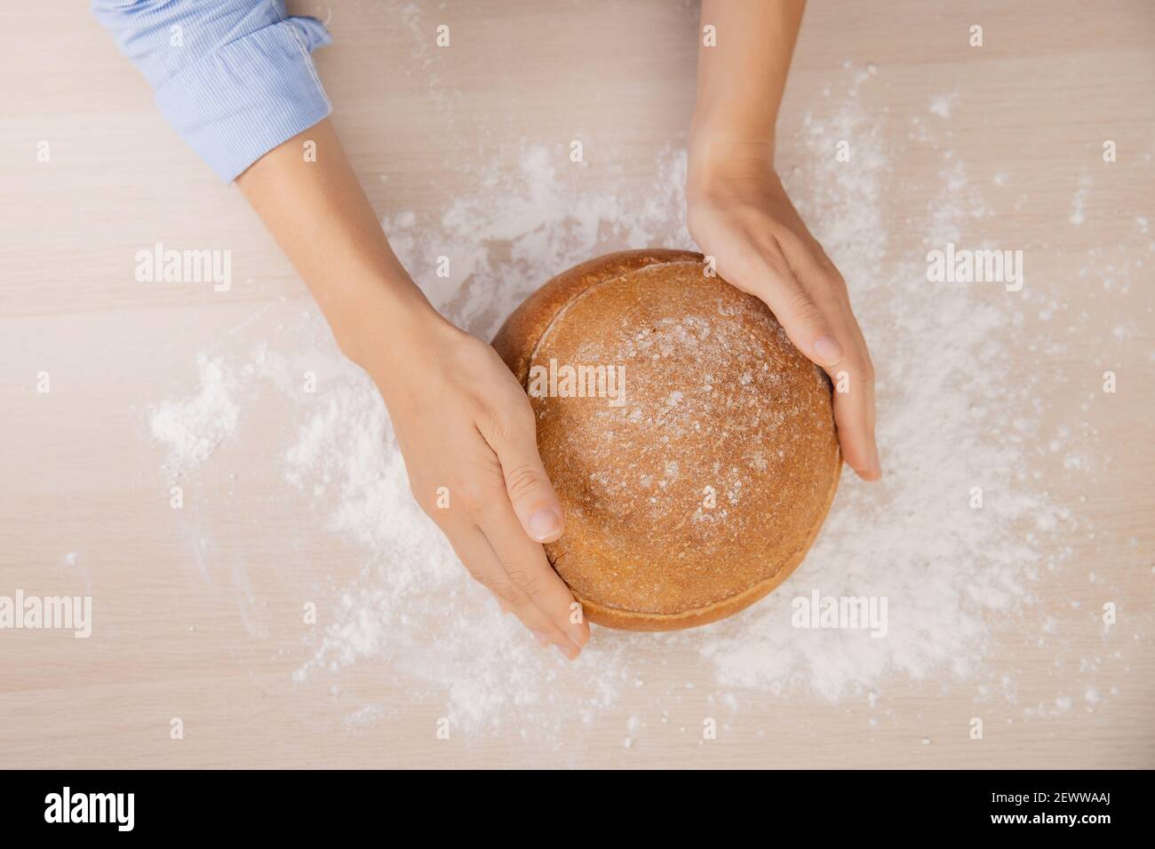Baker hand wheaten Round loaf of bread lies on table with flour, white kitchen background top view. Stock Photo