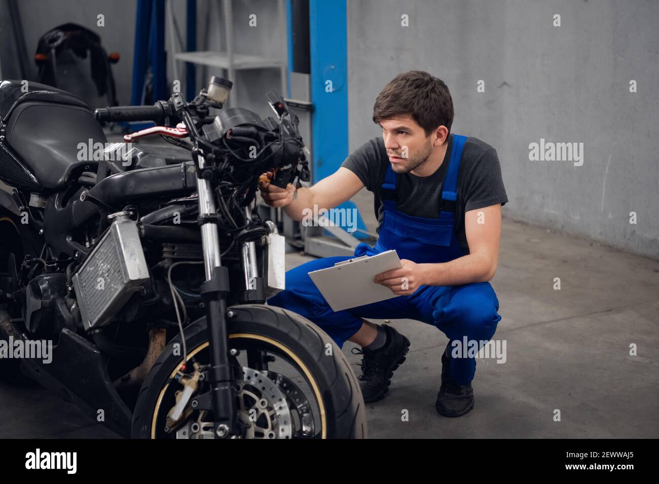 Worker in blue overalls examines a motorcycle Stock Photo - Alamy