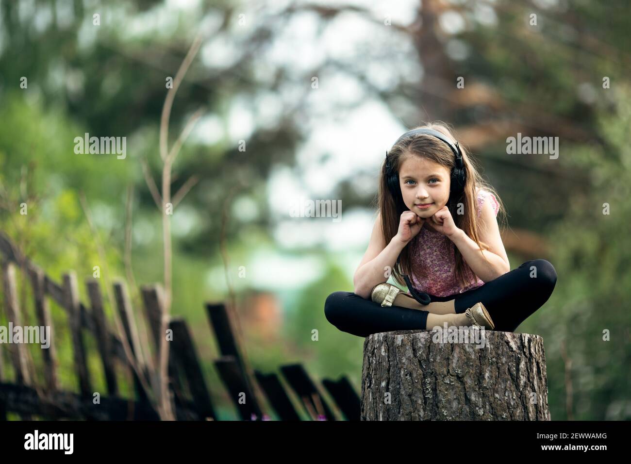 Little girl in headphones sitting on a stump in the village Stock Photo ...
